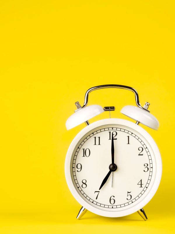 White alarm clock on a yellow background isolated, close-up. Minimal creative concept.